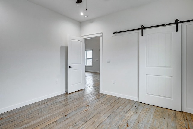 unfurnished bedroom with a barn door, light wood-style flooring, and baseboards