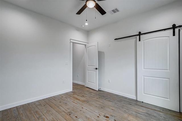 unfurnished bedroom with light wood-type flooring, a barn door, visible vents, and baseboards