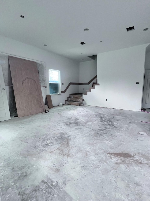unfurnished living room featuring stairway and unfinished concrete floors