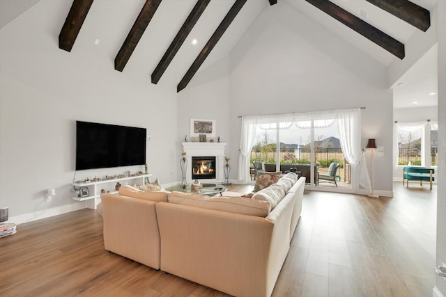 living room featuring light wood-type flooring, a glass covered fireplace, beam ceiling, and baseboards