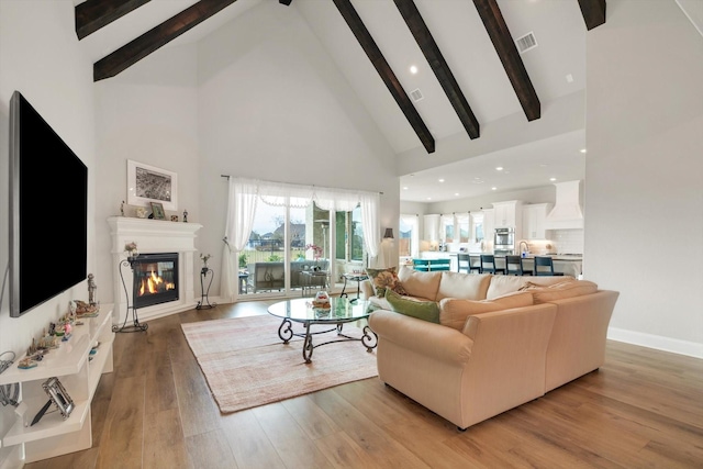 living area with visible vents, a glass covered fireplace, light wood-style flooring, high vaulted ceiling, and beam ceiling