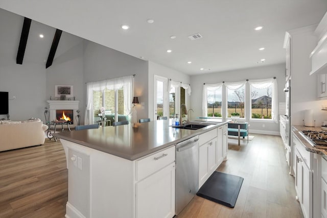 kitchen with a kitchen island with sink, stainless steel appliances, a sink, visible vents, and white cabinets