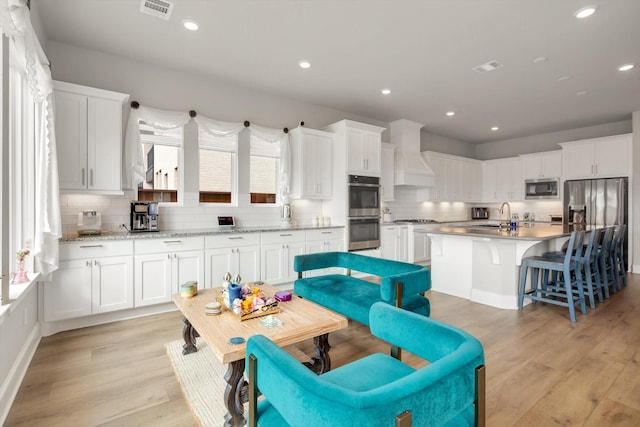 kitchen with a center island, visible vents, appliances with stainless steel finishes, white cabinetry, and premium range hood