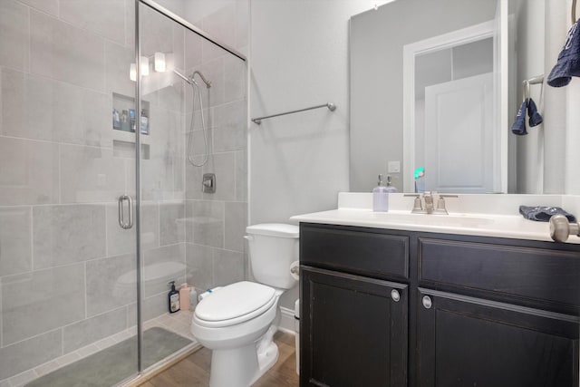 bathroom with toilet, wood finished floors, a shower stall, and vanity