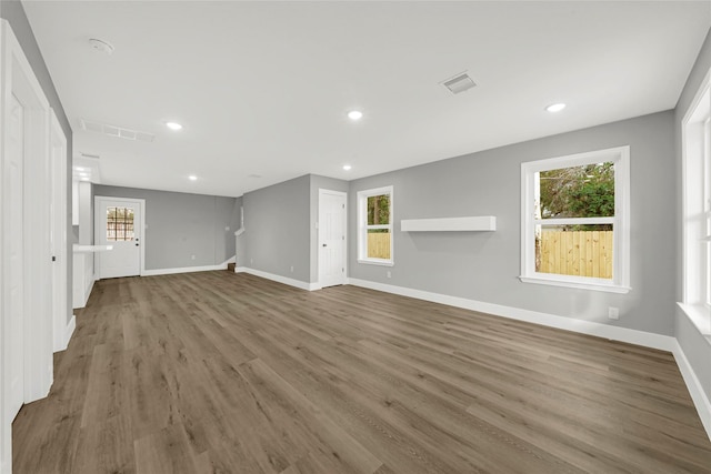 unfurnished living room with stairway, baseboards, visible vents, and wood finished floors