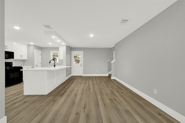 kitchen featuring visible vents, a peninsula, light countertops, black appliances, and white cabinetry