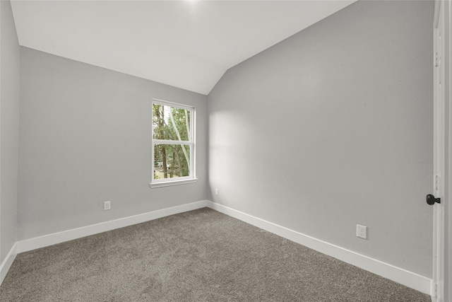 carpeted spare room featuring vaulted ceiling and baseboards