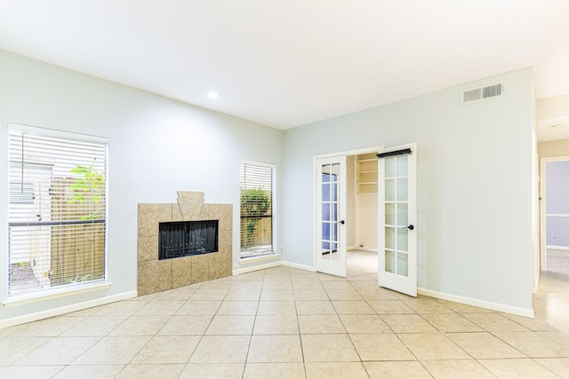 unfurnished living room with baseboards, visible vents, a tiled fireplace, french doors, and light tile patterned flooring