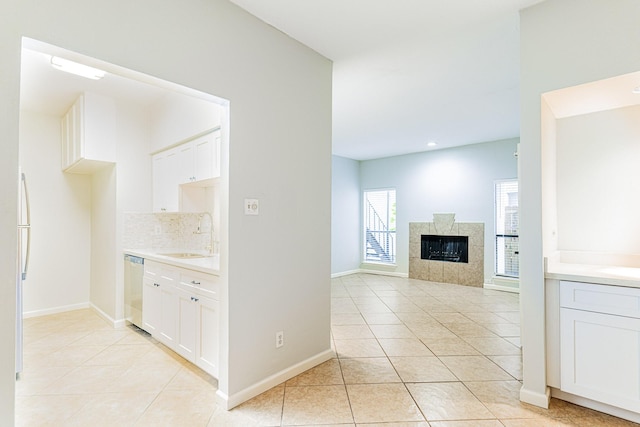 kitchen with light tile patterned floors, a tile fireplace, light countertops, white cabinetry, and a sink