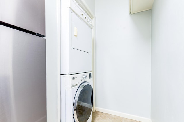 laundry area featuring laundry area, baseboards, stacked washing maching and dryer, and light tile patterned floors