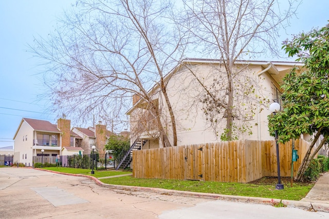 view of side of home with stucco siding, fence, and stairs