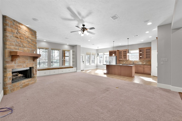 unfurnished living room with a textured ceiling, visible vents, a stone fireplace, and light colored carpet