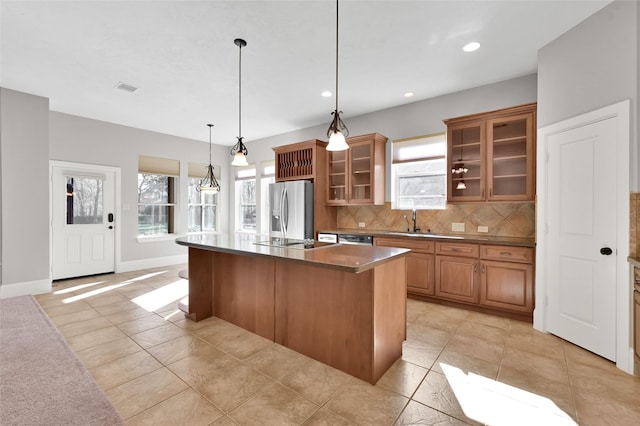 kitchen featuring tasteful backsplash, dark countertops, glass insert cabinets, appliances with stainless steel finishes, and a kitchen island