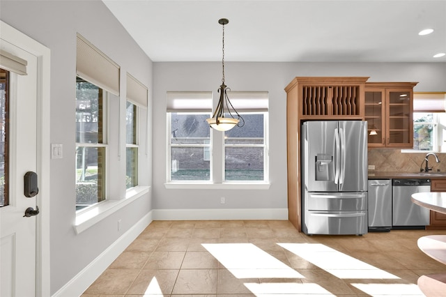 kitchen featuring decorative light fixtures, stainless steel appliances, dark countertops, glass insert cabinets, and a sink