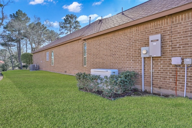 view of side of property featuring a shingled roof, brick siding, a lawn, and central AC unit