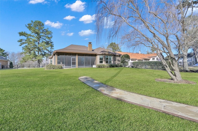 rear view of property with a sunroom, a yard, a chimney, and fence