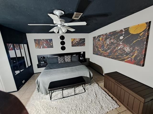 bedroom with a textured ceiling, light tile patterned flooring, visible vents, and a ceiling fan