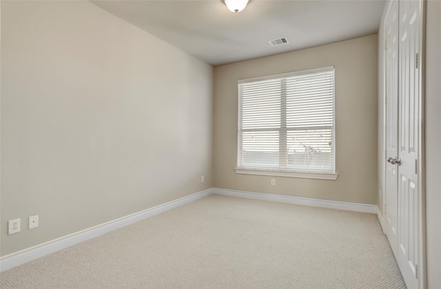 spare room with light colored carpet, visible vents, and baseboards