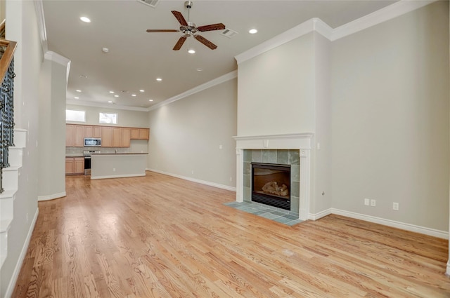 unfurnished living room with light wood finished floors, visible vents, ornamental molding, a tile fireplace, and baseboards