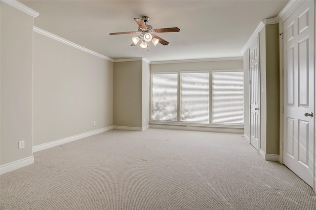 empty room with ornamental molding, light carpet, baseboards, and a ceiling fan