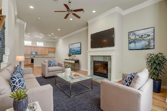 living area featuring a tiled fireplace, light wood-type flooring, visible vents, and crown molding