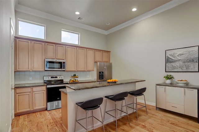 kitchen with light wood finished floors, visible vents, decorative backsplash, appliances with stainless steel finishes, and a kitchen breakfast bar