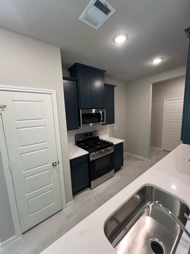 kitchen with stainless steel appliances, light countertops, visible vents, backsplash, and a sink