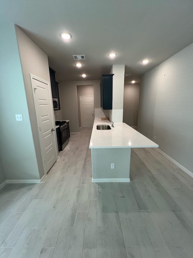 kitchen with a sink, visible vents, light wood-style floors, light countertops, and dark cabinetry