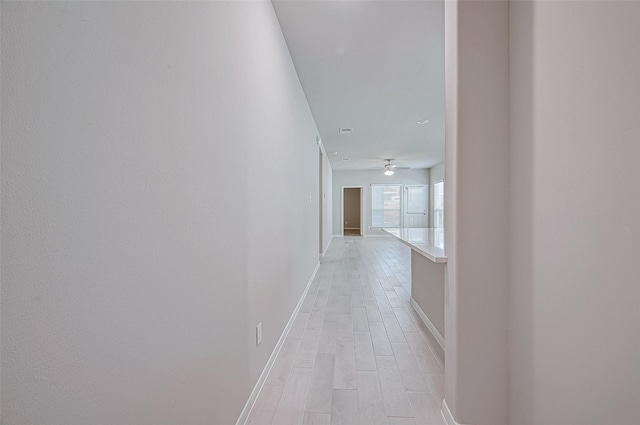 corridor featuring light wood finished floors and baseboards