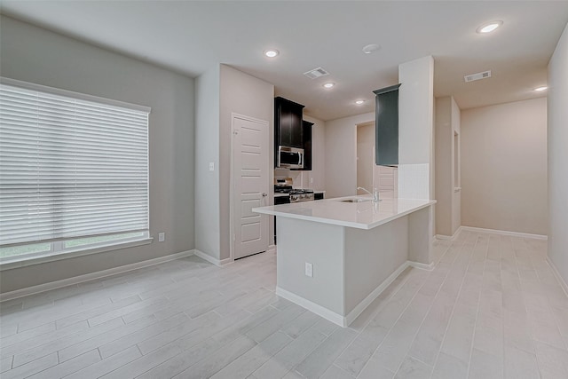 kitchen featuring visible vents, stainless steel appliances, light countertops, dark cabinetry, and a sink