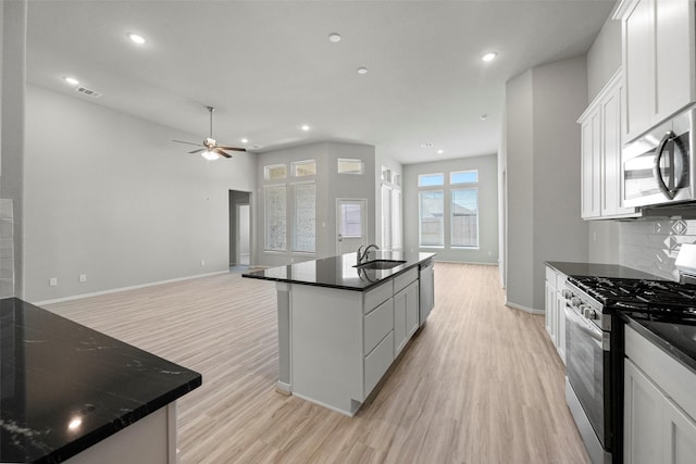 kitchen featuring visible vents, white cabinets, dark countertops, an island with sink, and stainless steel appliances