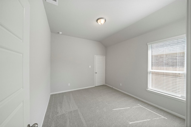 carpeted spare room featuring lofted ceiling and baseboards