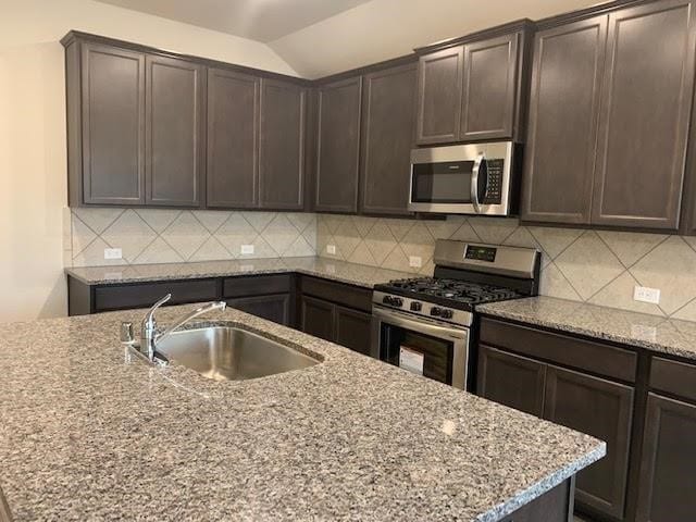 kitchen featuring stainless steel appliances, a sink, dark brown cabinetry, and light stone countertops