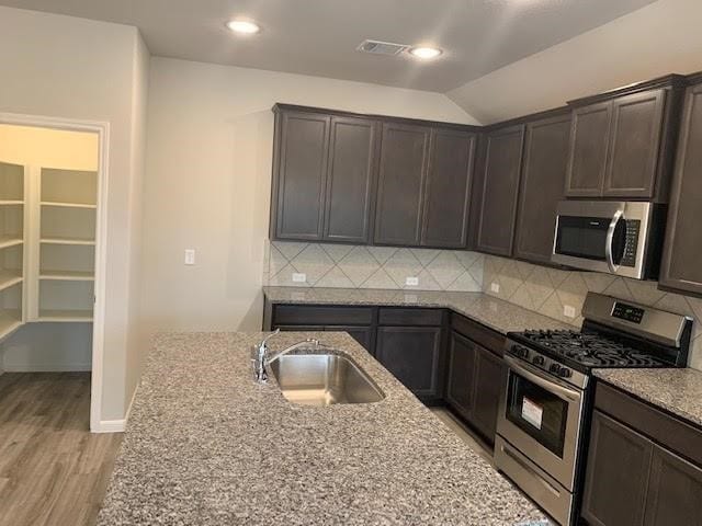 kitchen featuring stainless steel appliances, light stone counters, a sink, and dark brown cabinetry