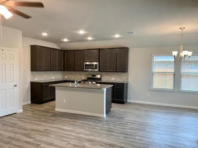 kitchen with pendant lighting, a center island with sink, stainless steel appliances, lofted ceiling, and light countertops