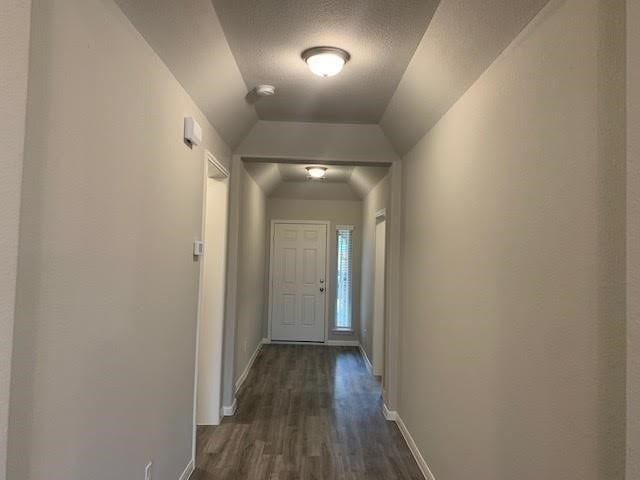 doorway featuring dark wood-style floors, lofted ceiling, a textured ceiling, and baseboards