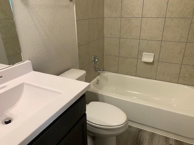 full bathroom featuring a textured wall, vanity, toilet, and wood finished floors