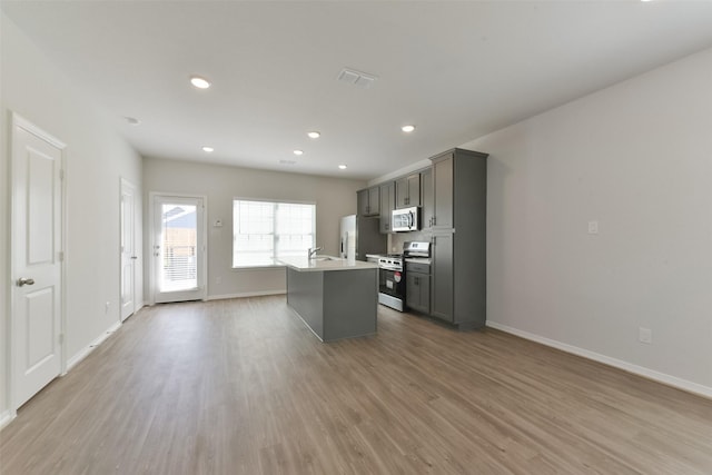 6835 New York St, Houston, TX 77021 - kitchen with stainless steel appliances, a sink, wood finished floors, baseboards, and an island with sink