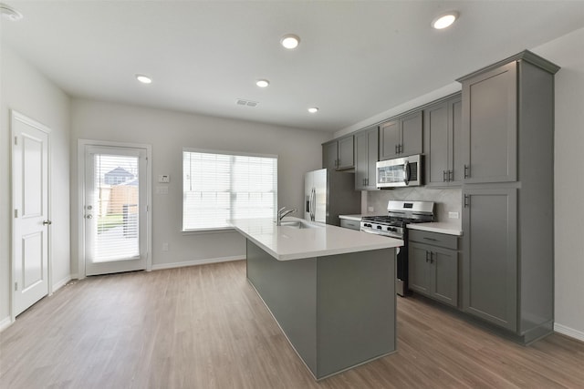 6835 New York St, Houston, TX 77021 - kitchen featuring an island with sink, stainless steel appliances, gray cabinetry, light wood-style floors, and a sink