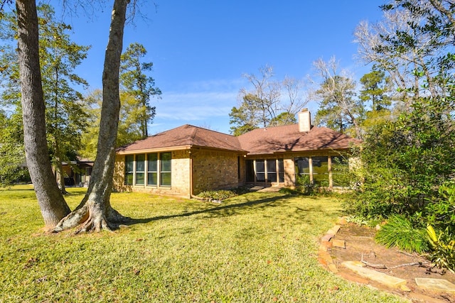 back of property with brick siding, a chimney, and a yard