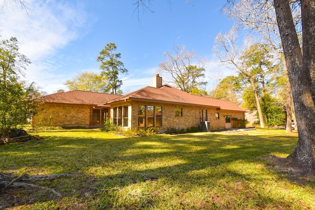 back of property featuring brick siding, a lawn, and a chimney