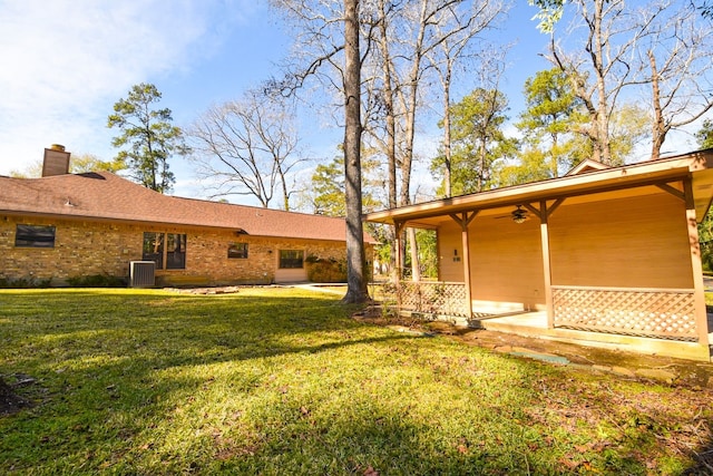 exterior space featuring brick siding, a chimney, a lawn, a ceiling fan, and cooling unit