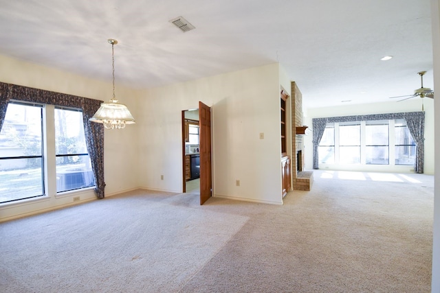 empty room with light colored carpet, a fireplace, a ceiling fan, baseboards, and visible vents