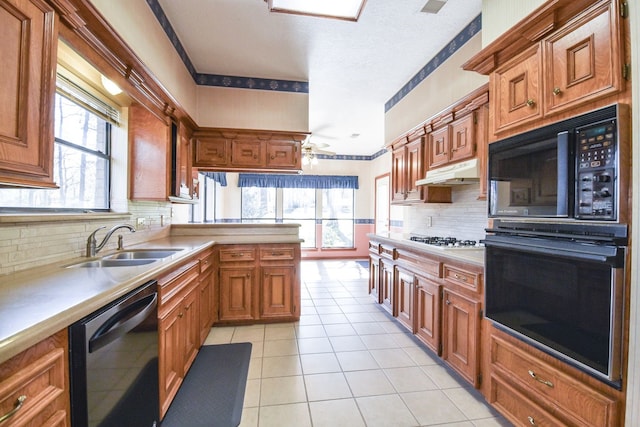 kitchen with brown cabinetry, under cabinet range hood, light countertops, black appliances, and a sink