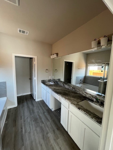 bathroom with a garden tub, double vanity, wood finished floors, and a sink