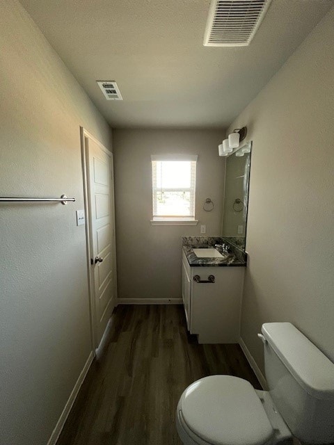 half bath featuring visible vents, vanity, toilet, and wood finished floors