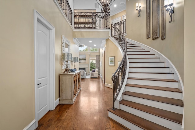 stairs with wood finished floors, recessed lighting, a fireplace, baseboards, and a towering ceiling