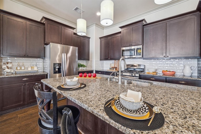 kitchen with a kitchen bar, a sink, dark wood finished floors, appliances with stainless steel finishes, and light stone countertops