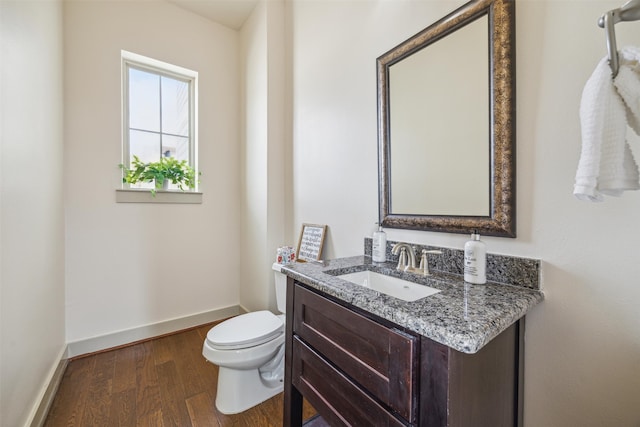 half bathroom featuring vanity, toilet, wood finished floors, and baseboards