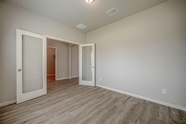 unfurnished room with light wood-style floors, french doors, visible vents, and baseboards